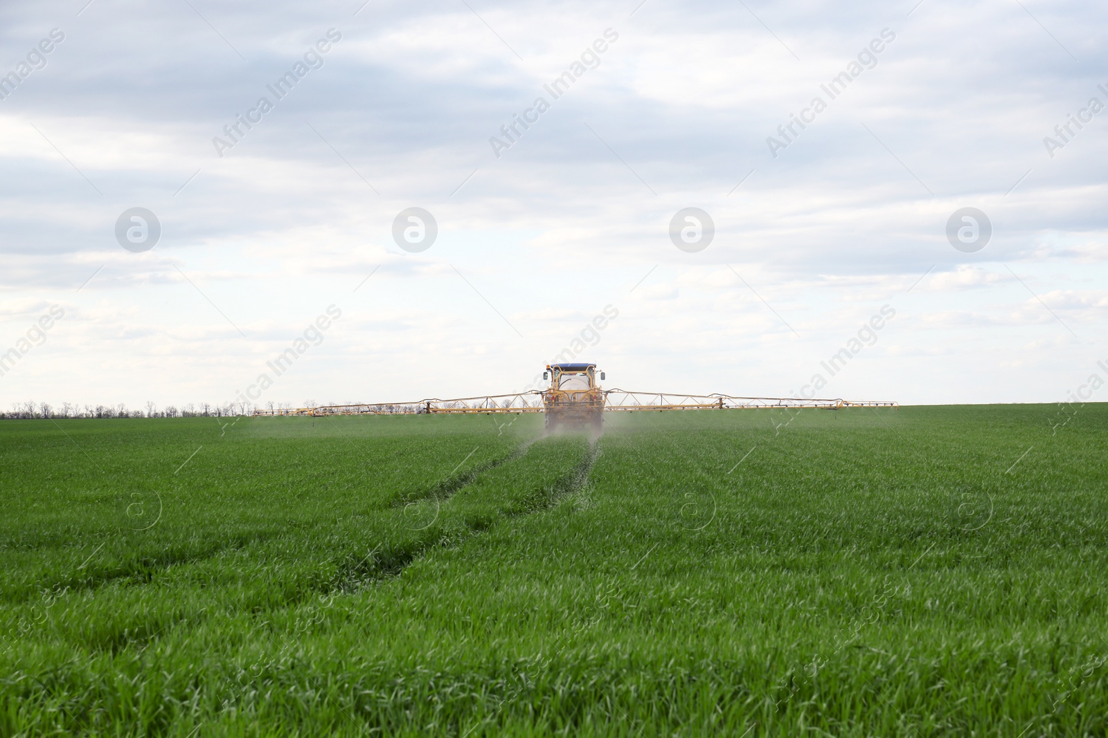 Photo of Tractor spraying pesticide in field on sunny day. Agricultural industry