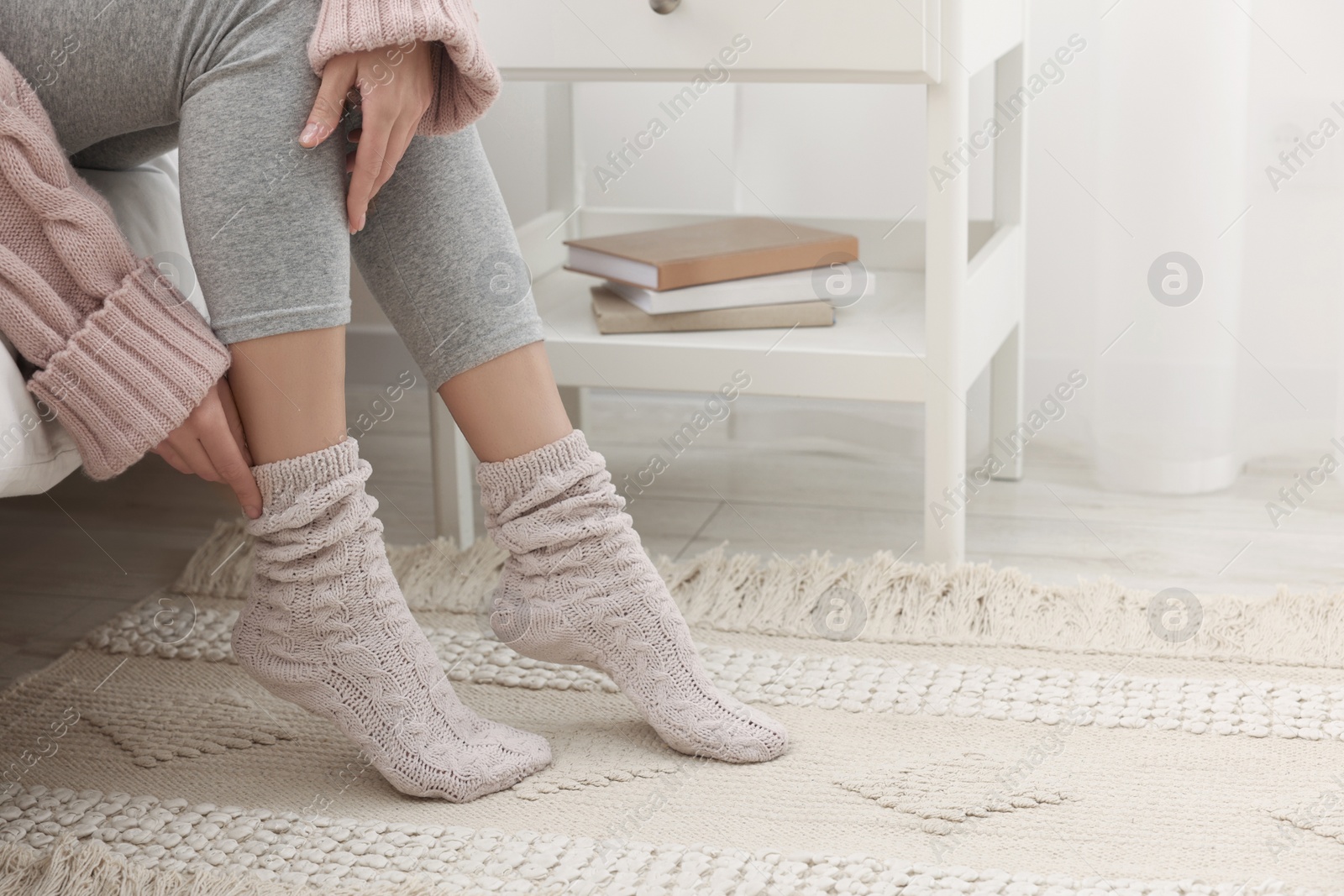 Photo of Woman wearing warm knitted socks at home, closeup. Space for text