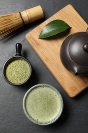 Cup of fresh matcha tea, bamboo whisk, teapot and green powder on black table, flat lay