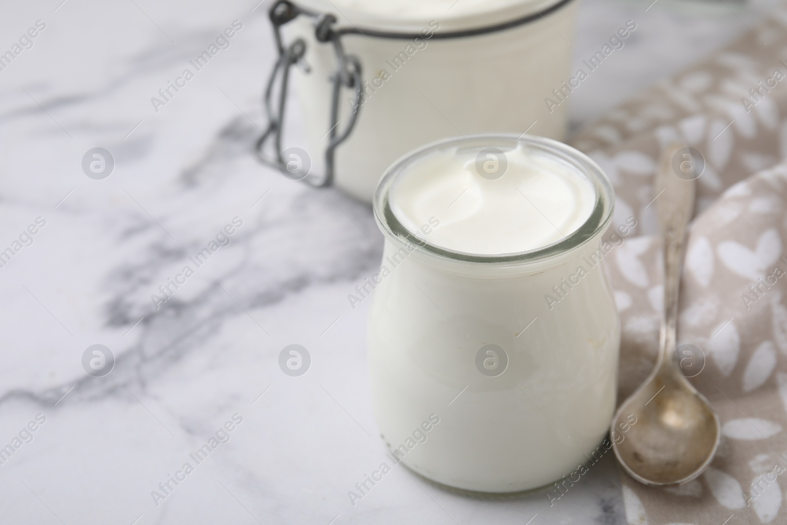 Photo of Delicious natural yogurt in glass jar and spoon on white marble table, closeup. Space for text