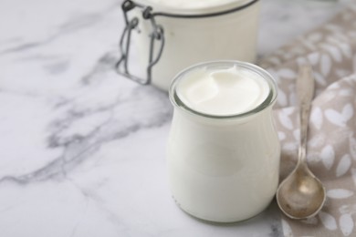 Photo of Delicious natural yogurt in glass jar and spoon on white marble table, closeup. Space for text