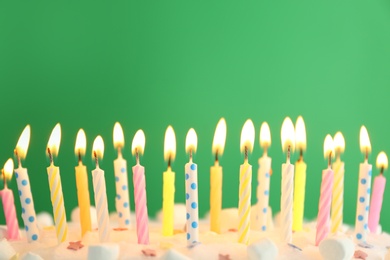 Birthday cake with burning candles on green background, closeup