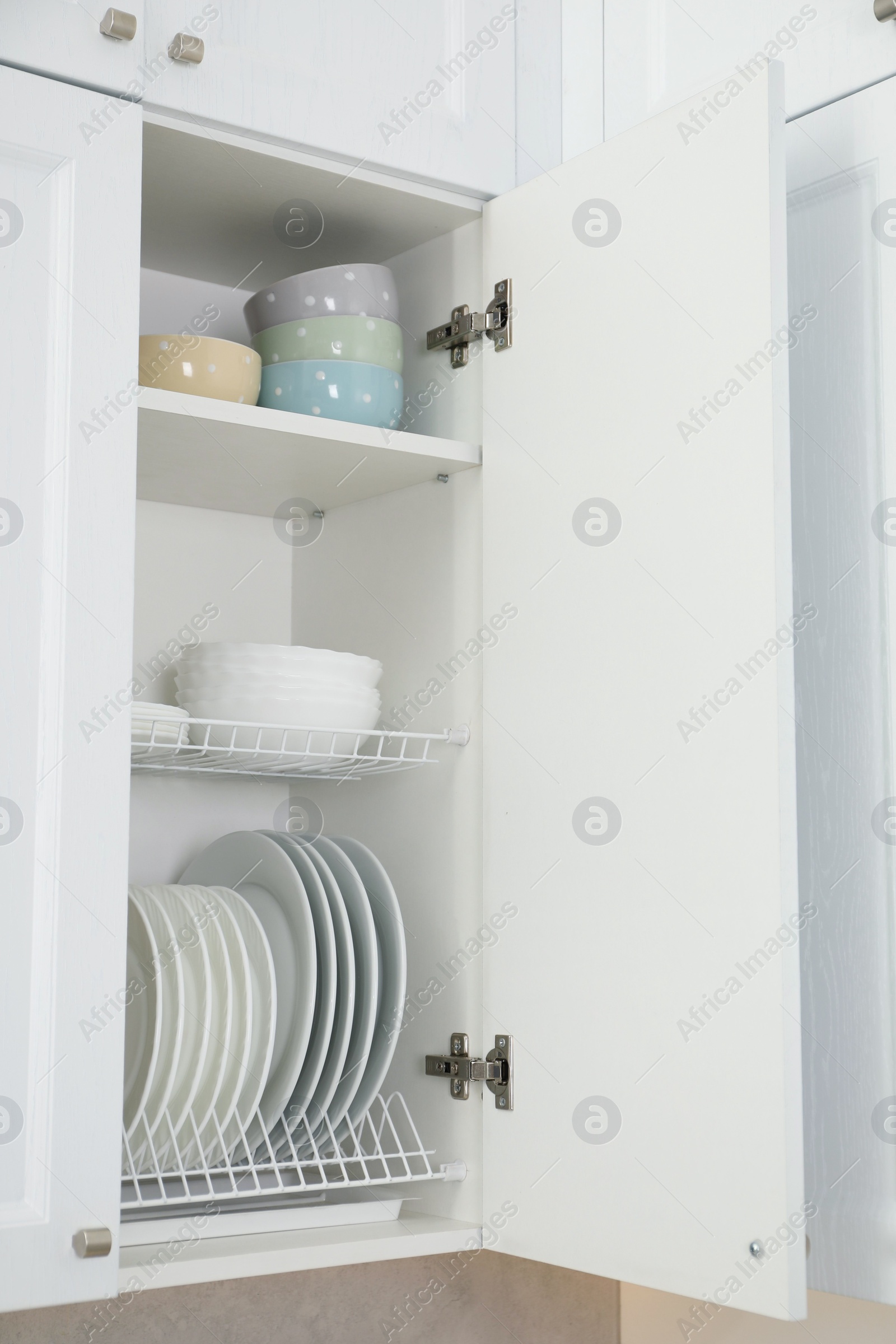 Photo of Clean plates and bowls on shelves in cabinet indoors