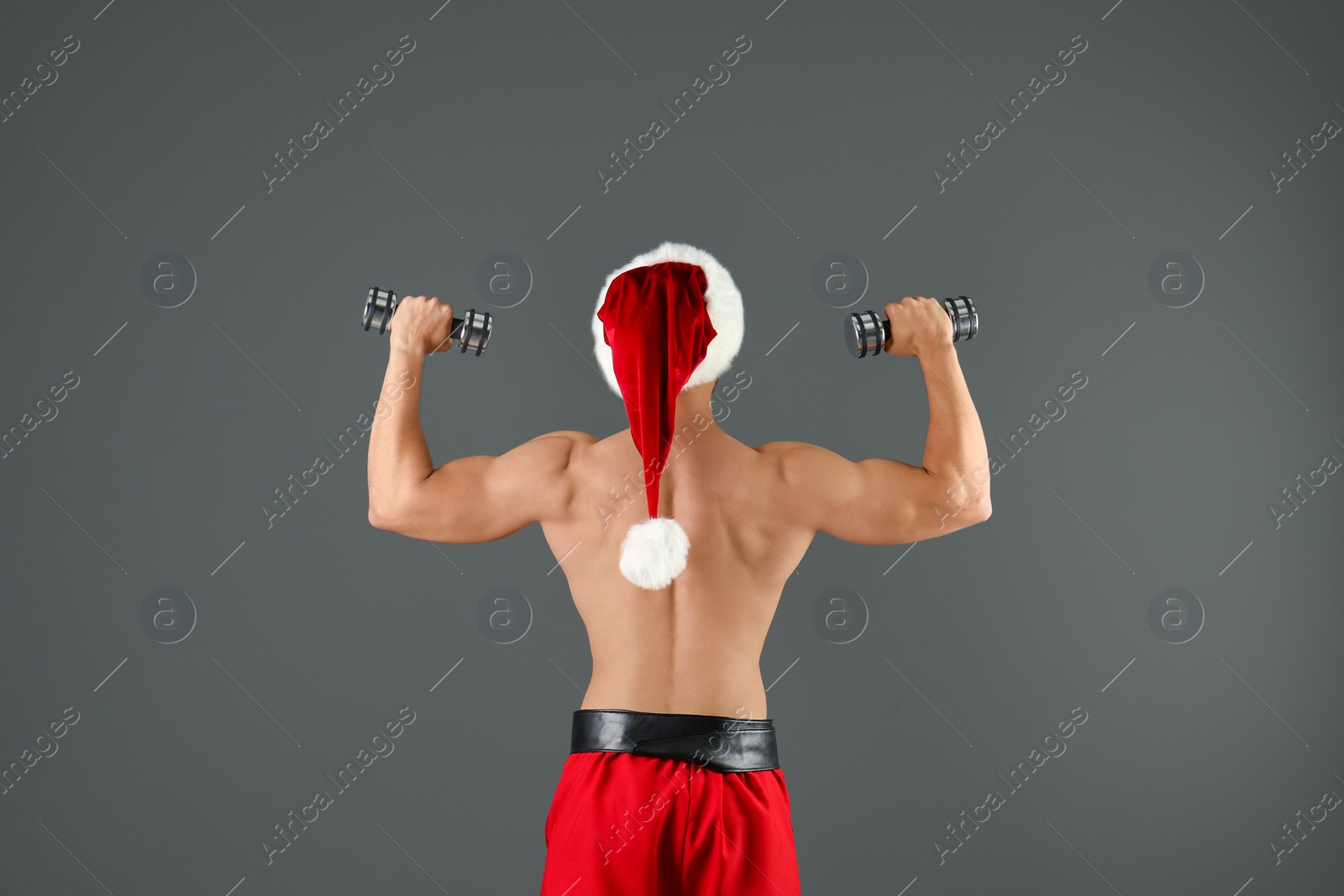 Photo of Shirtless sexy young Santa Claus with dumbbells on color background