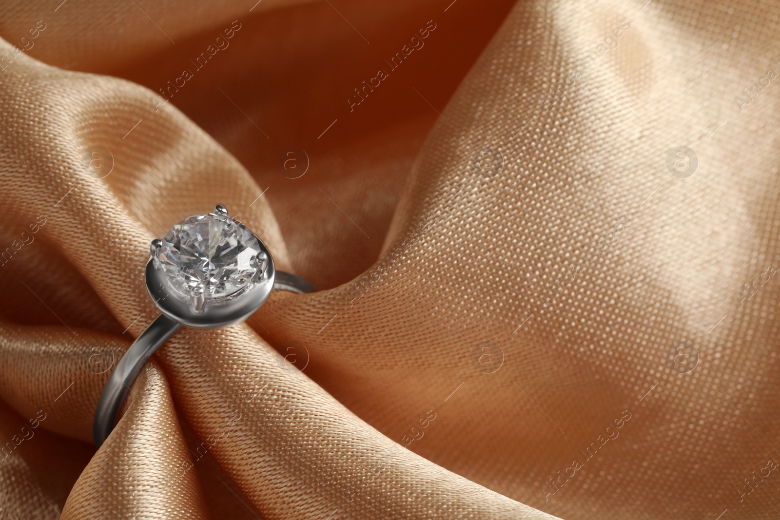 Photo of Beautiful luxury engagement ring with gemstone on beige fabric, closeup