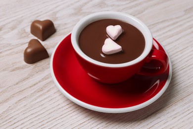 Cup of hot chocolate with heart shaped marshmallows and tasty candies on white wooden table