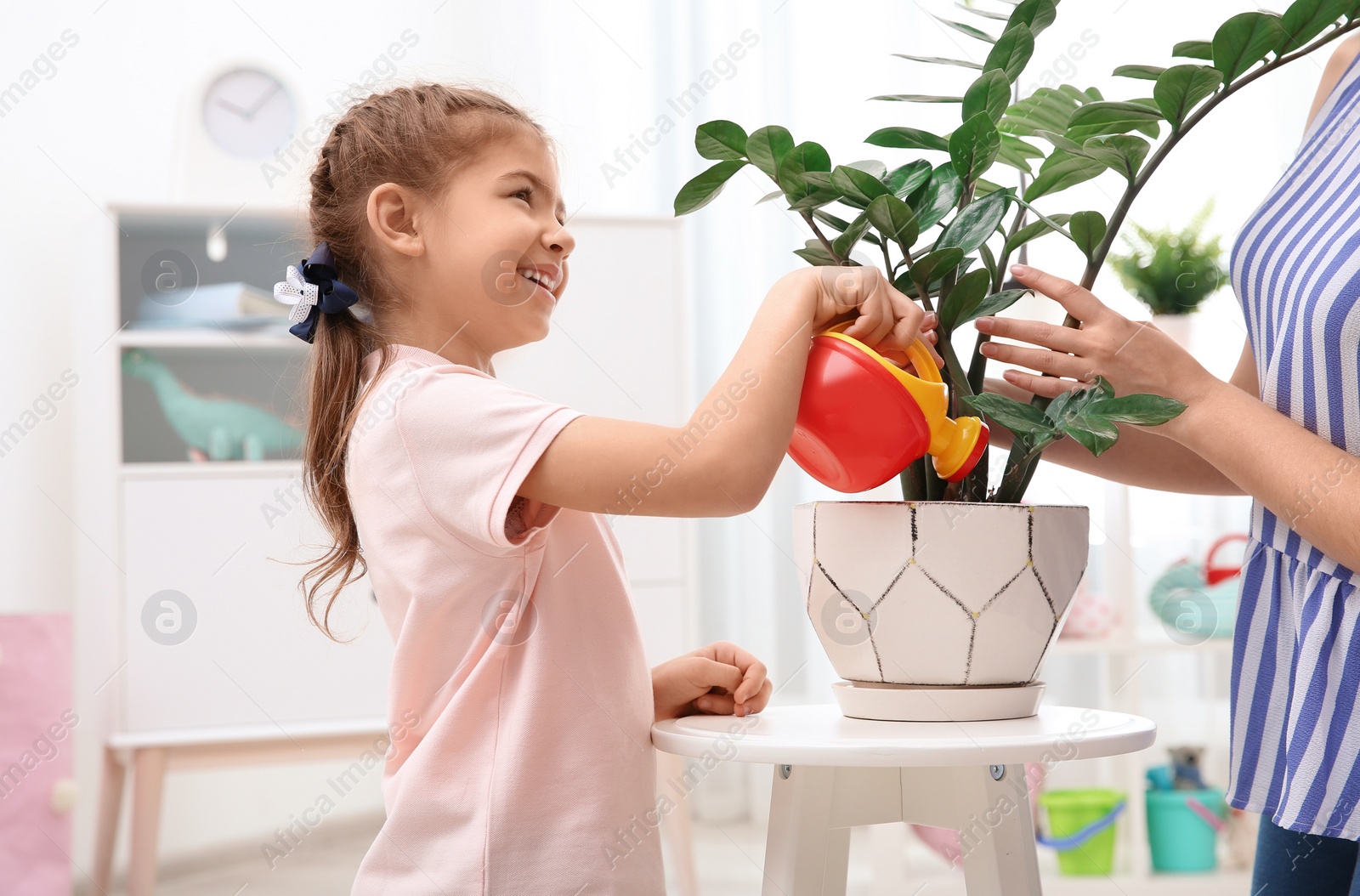 Photo of Child with toy watering can helping mother to take care of houseplant at home. Playing indoors