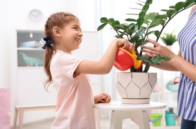 Child with toy watering can helping mother to take care of houseplant at home. Playing indoors