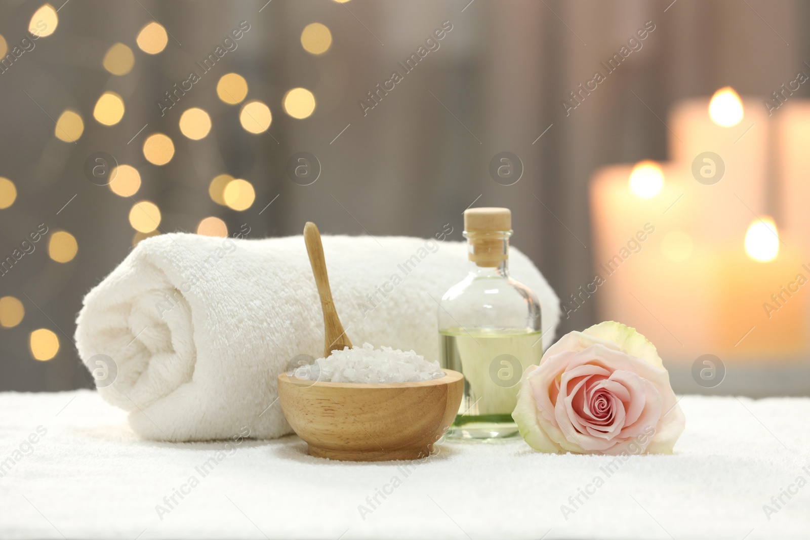 Photo of Beautiful spa composition with essential oil, sea salt and rose on white towel against blurred lights