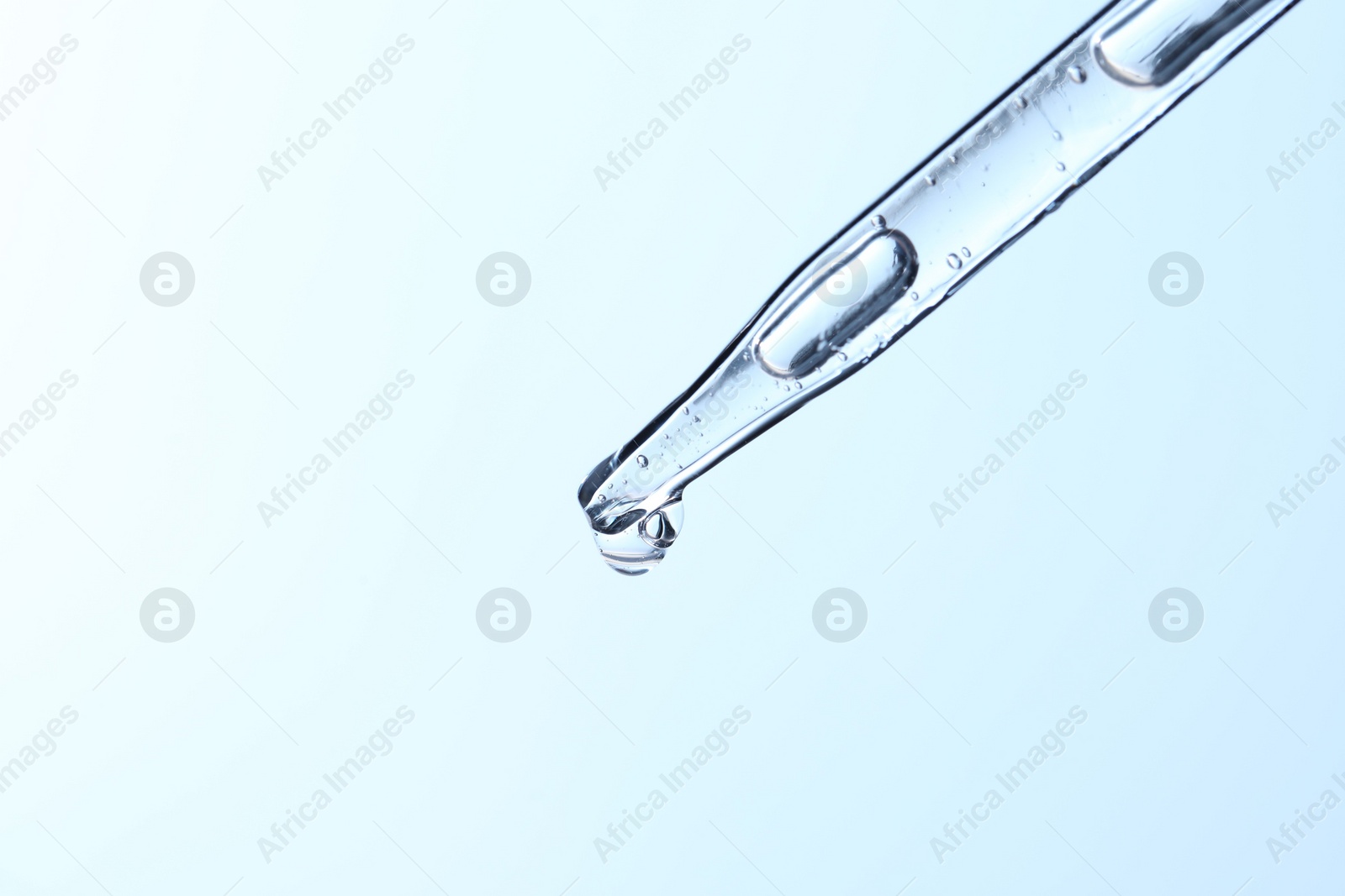 Photo of Dripping liquid from pipette on light blue background, closeup