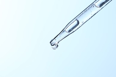 Dripping liquid from pipette on light blue background, closeup