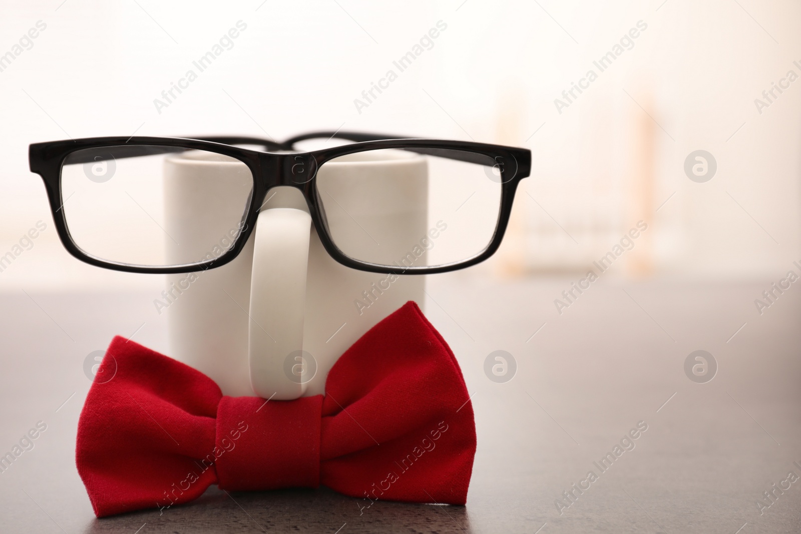 Photo of Funny composition with red bow tie, glasses and cup on grey table. Space for text