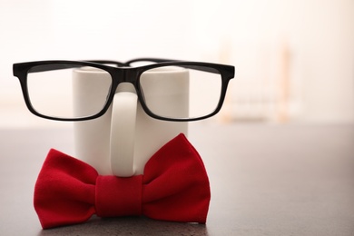 Photo of Funny composition with red bow tie, glasses and cup on grey table. Space for text