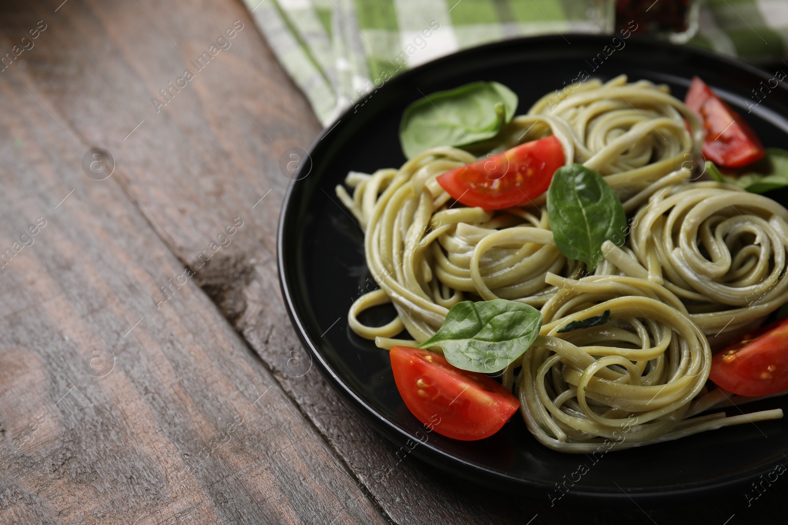 Photo of Tasty pasta with spinach, sauce and tomatoes on wooden table, space for text