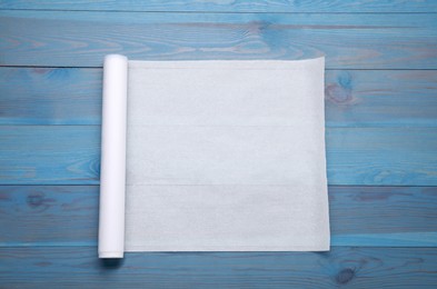 Roll of baking paper on light blue wooden table, top view