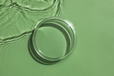 Photo of Stylish presentation for product. Glass podium in water on pale green background, top view