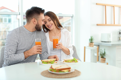 Happy couple having breakfast with sandwiches at table in kitchen