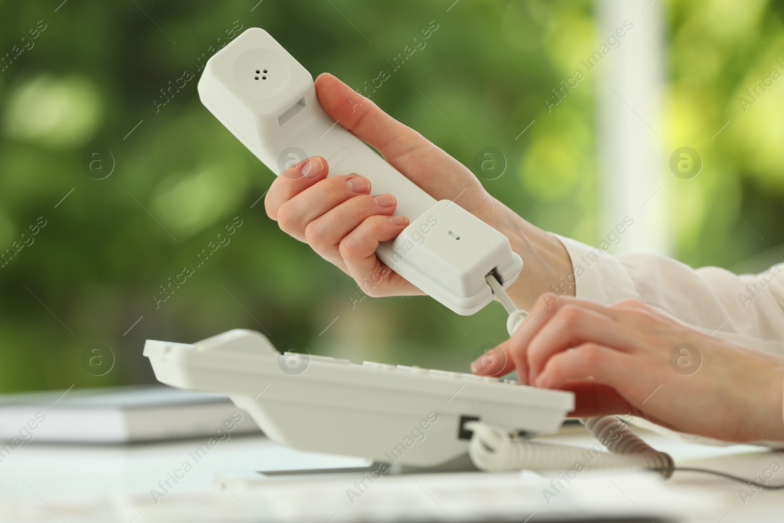 Photo of Assistant dialing number on telephone at white table, closeup