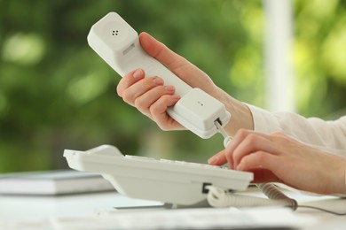 Photo of Assistant dialing number on telephone at white table, closeup