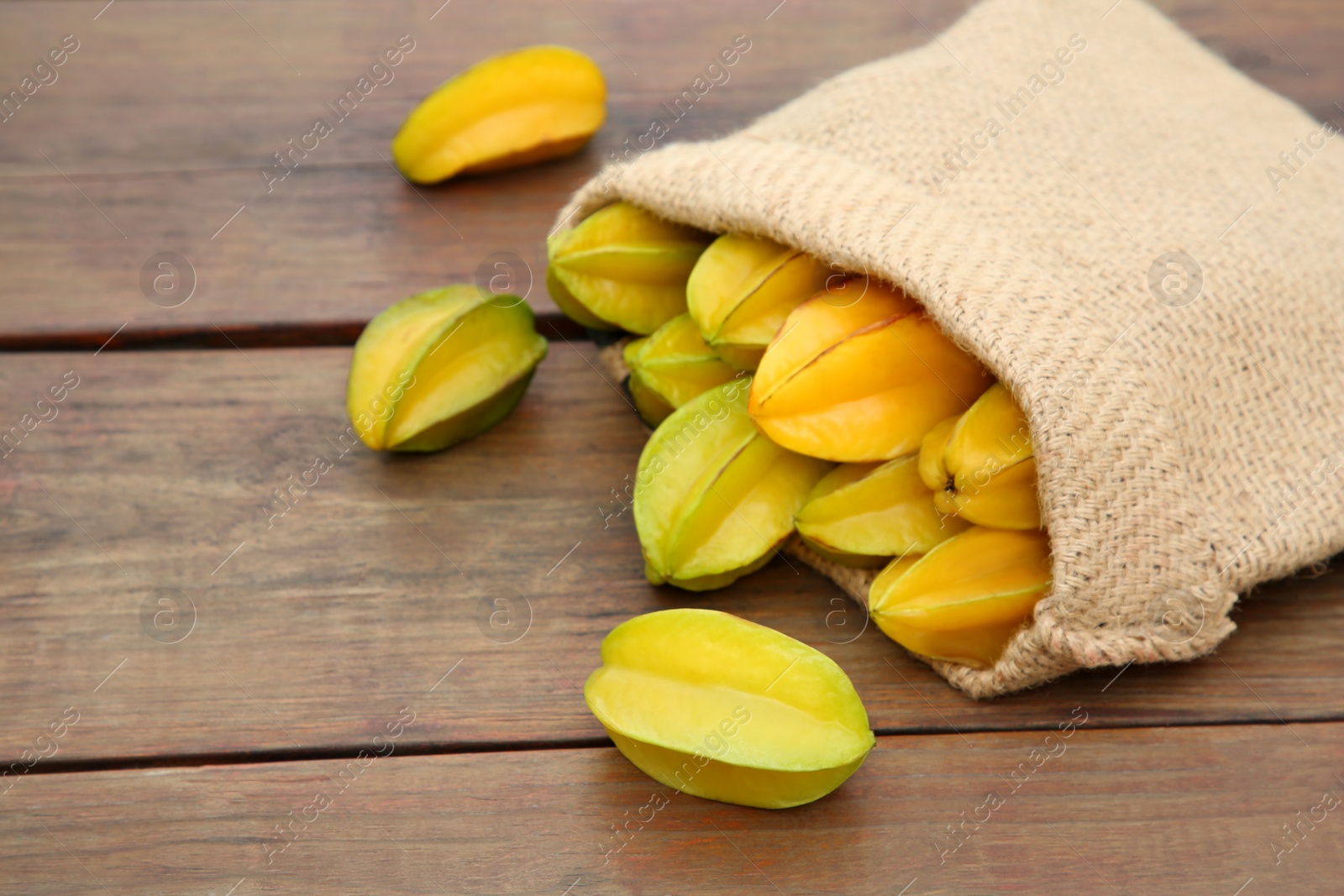 Photo of Sack with delicious ripe carambolas on wooden table