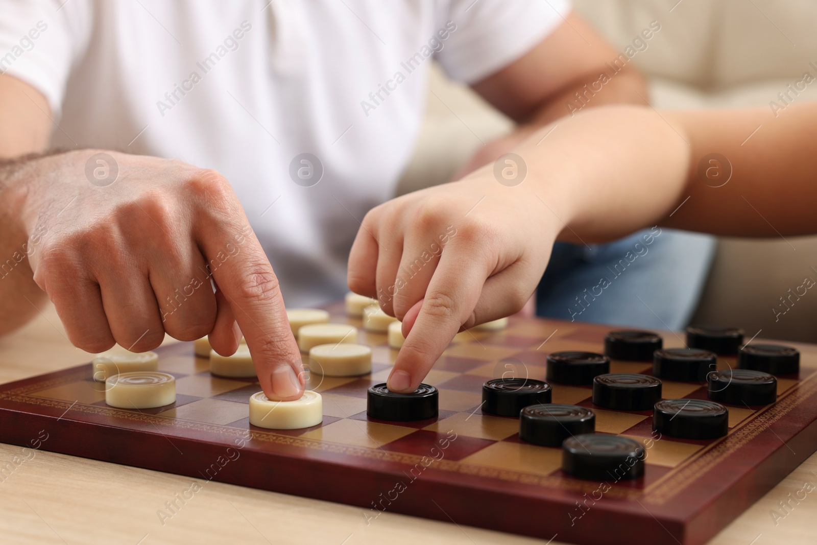 Photo of Father playing checkers with his son at table in room, closeup