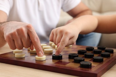Photo of Father playing checkers with his son at table in room, closeup