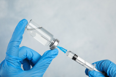 Photo of Doctor filling syringe with medication on light background, closeup. Vaccination and immunization