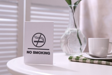 Photo of No Smoking sign and cup of coffee on white table indoors