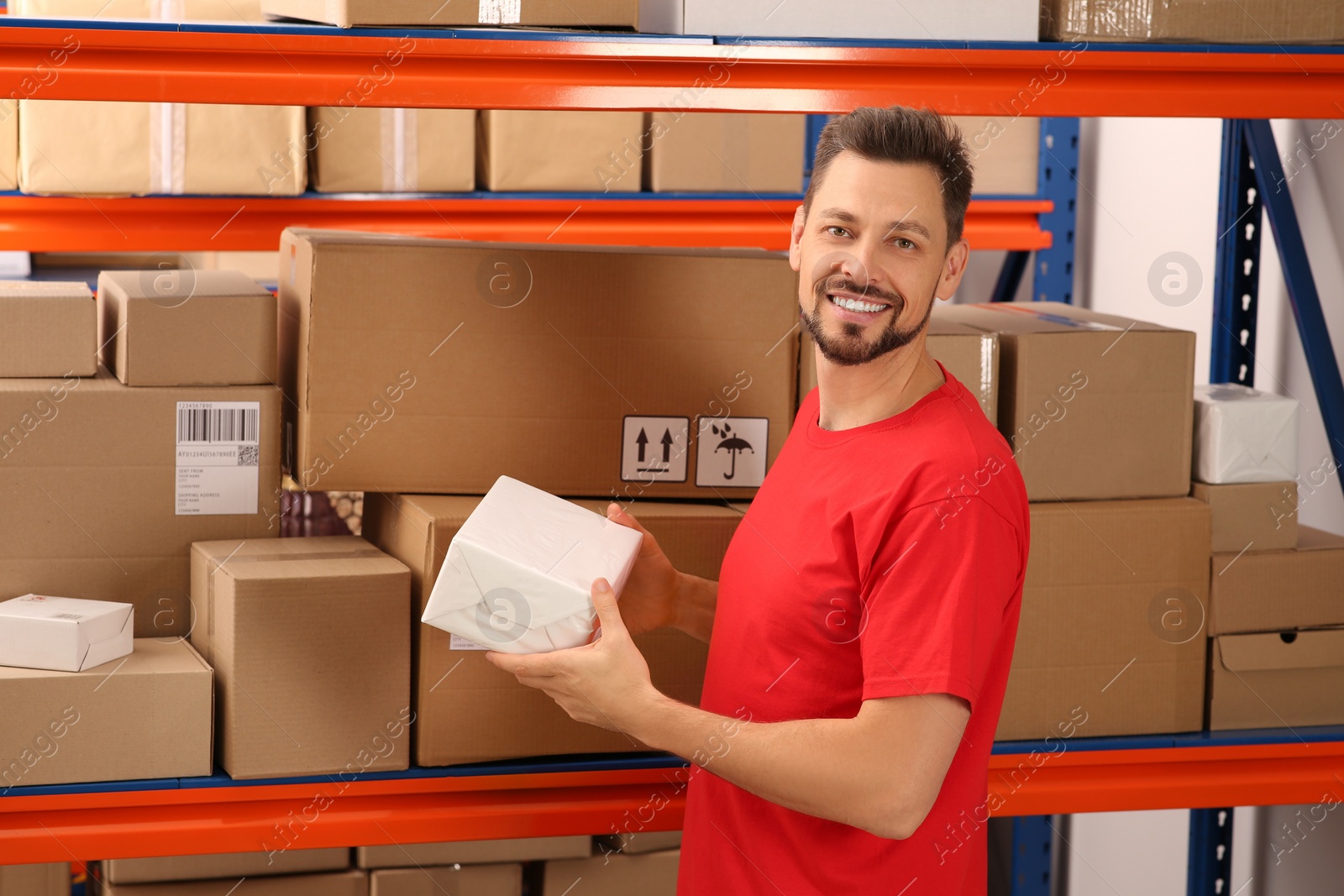 Photo of Post office worker holding box near rack with parcels indoors