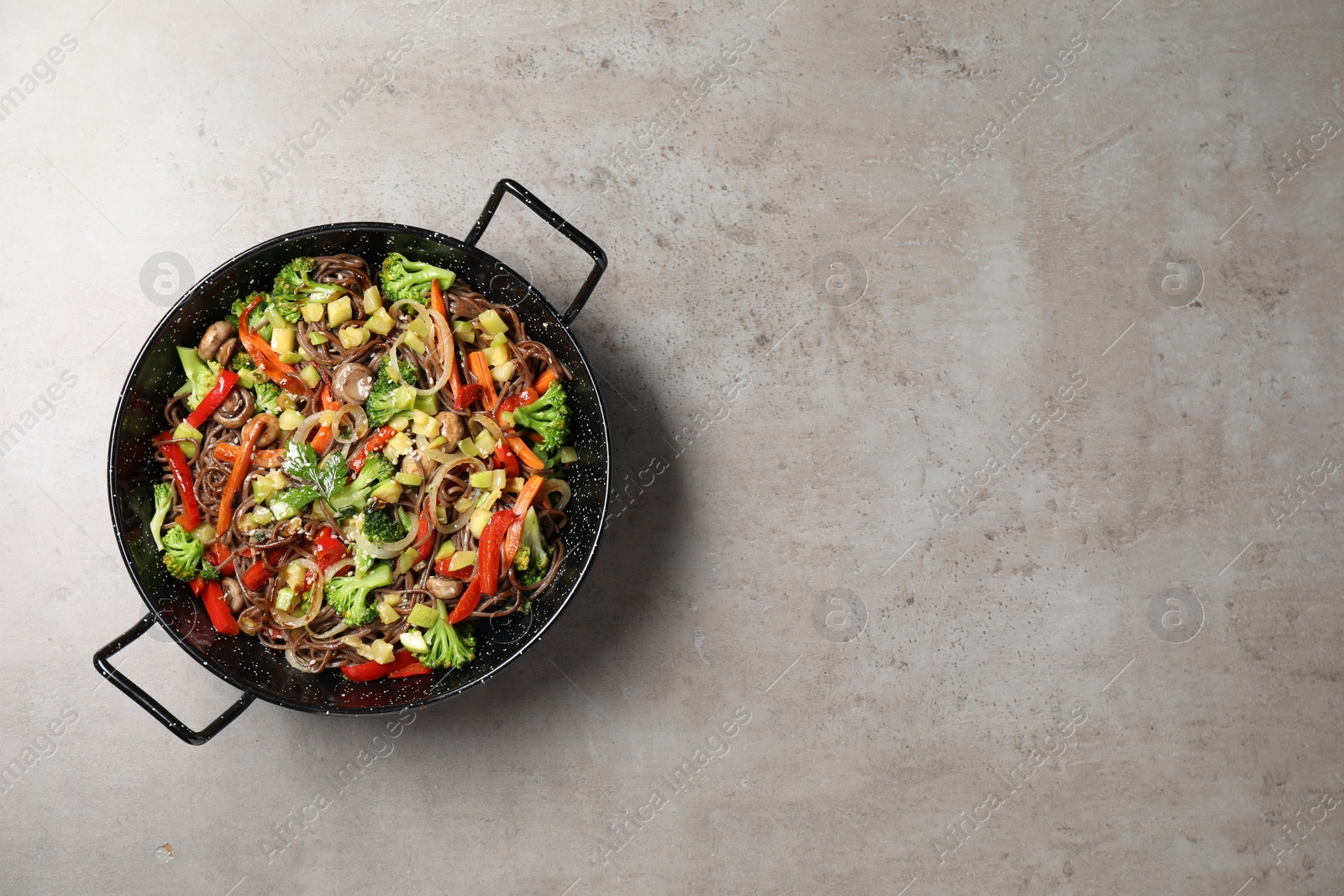 Photo of Stir-fry. Tasty noodles with meat and vegetables in wok on grey textured table, top view. Space for text