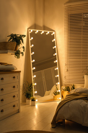 Photo of Stylish mirror with light bulbs in dark bedroom. Interior design