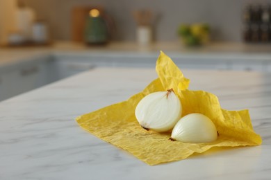 Photo of Halves of onion with yellow beeswax food wrap on white marble table, space for text