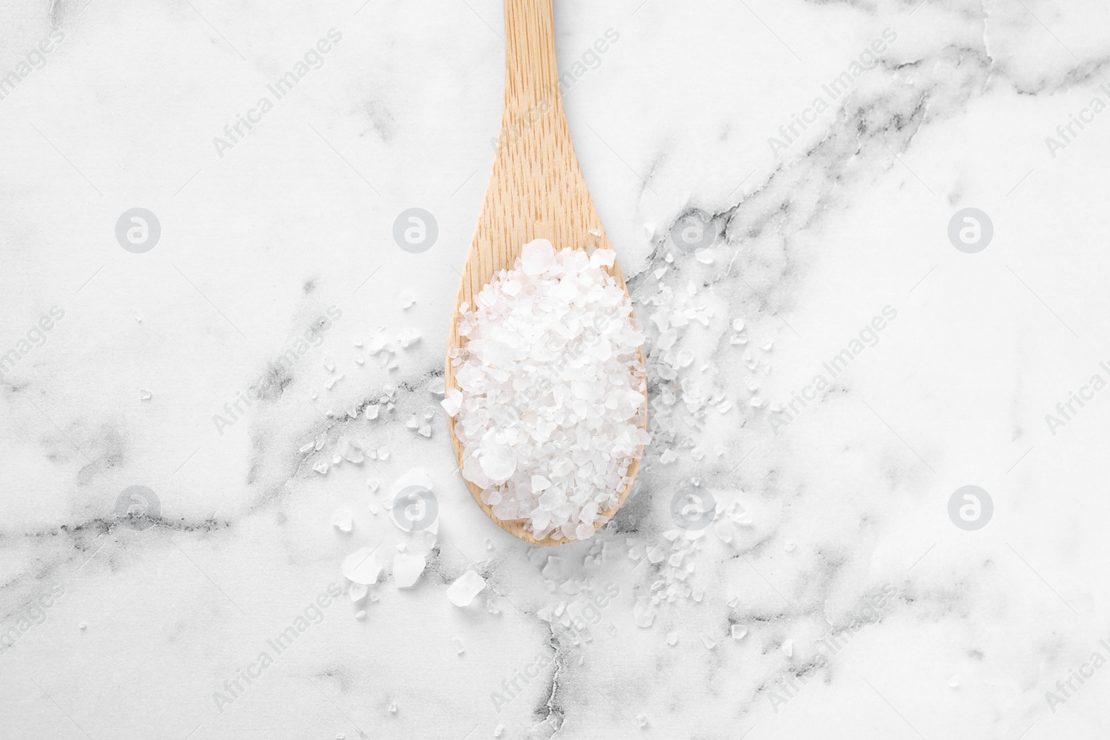 Photo of Spoon with white sea salt on marble table, top view. Spa treatment