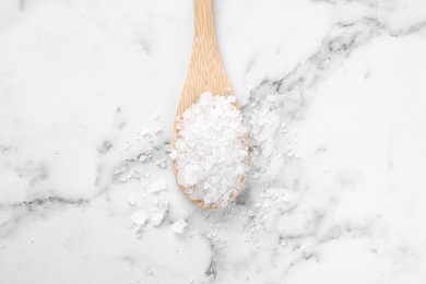 Photo of Spoon with white sea salt on marble table, top view. Spa treatment