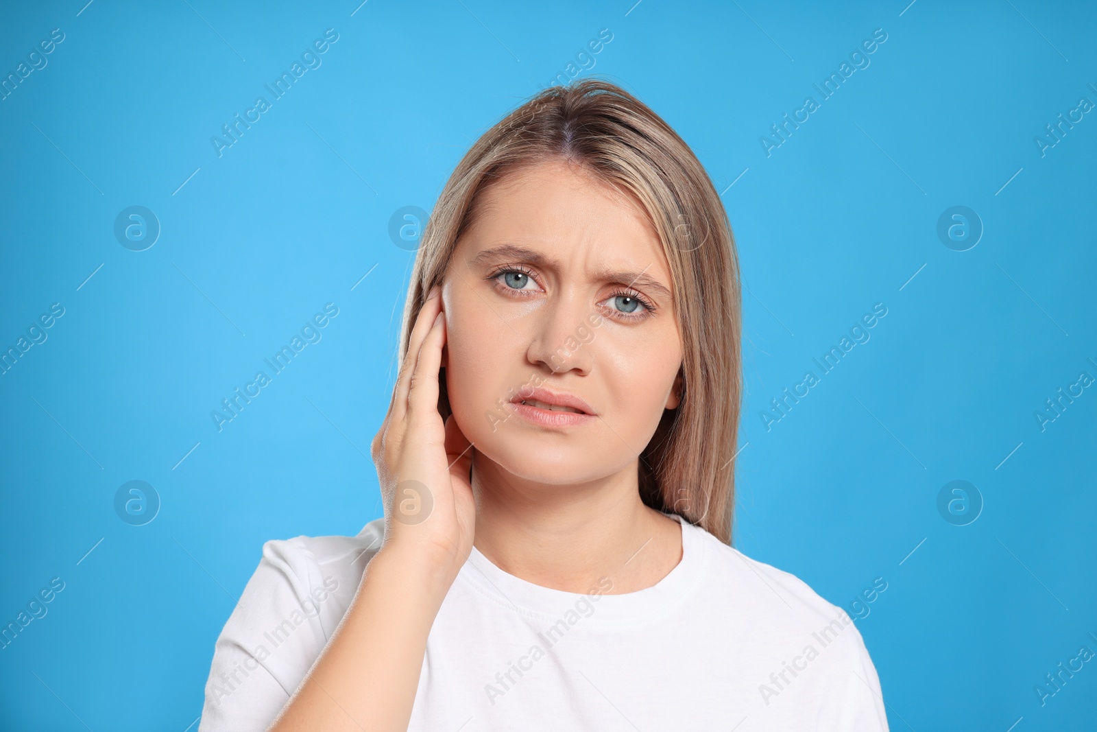 Photo of Young woman suffering from ear pain on light blue background