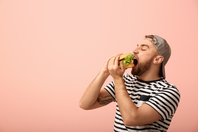 Young man eating tasty burger on color background. Space for text