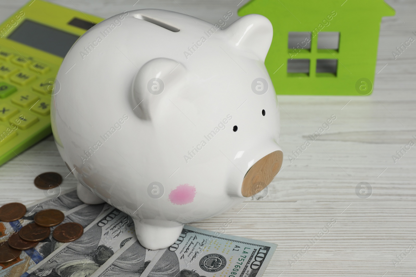 Photo of Piggy bank, house model, calculator and money on white wooden table, closeup. Space for text