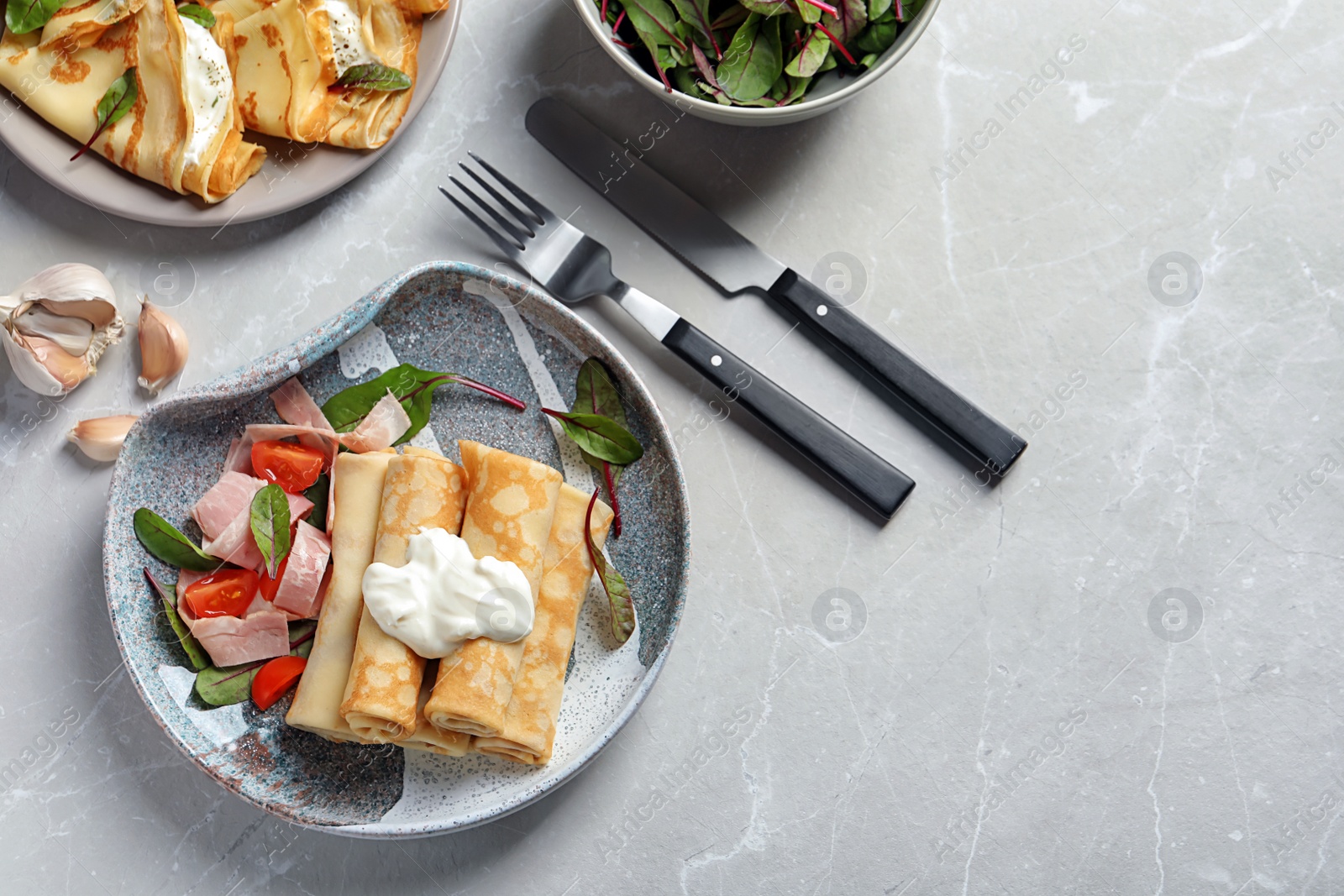 Photo of Thin pancakes served with sour cream and garnish on plates, top view