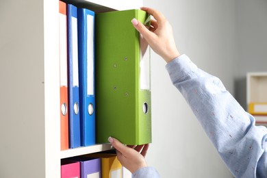 Photo of Woman taking binder office folder from shelving unit indoors, closeup