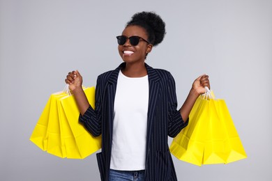 Happy young woman in stylish sunglasses with shopping bags on light grey background