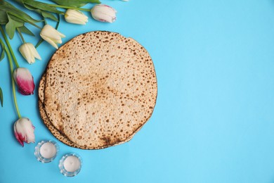 Photo of Tasty matzos, tulips and candles on light blue background, flat lay with space for text. Passover (Pesach) celebration