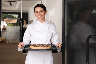 Photo of Happy baker presenting delicious quiche at door of her cafe