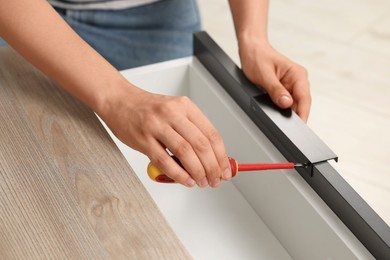 Photo of Woman with screwdriver assembling drawer, closeup view