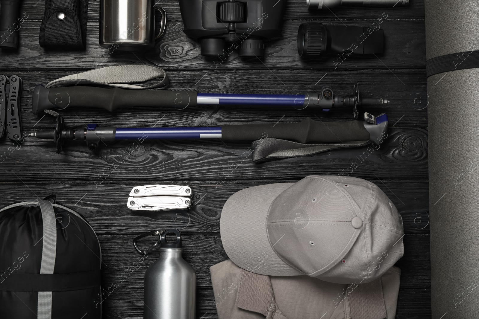 Photo of Flat lay composition with trekking poles and other hiking equipment on black wooden background