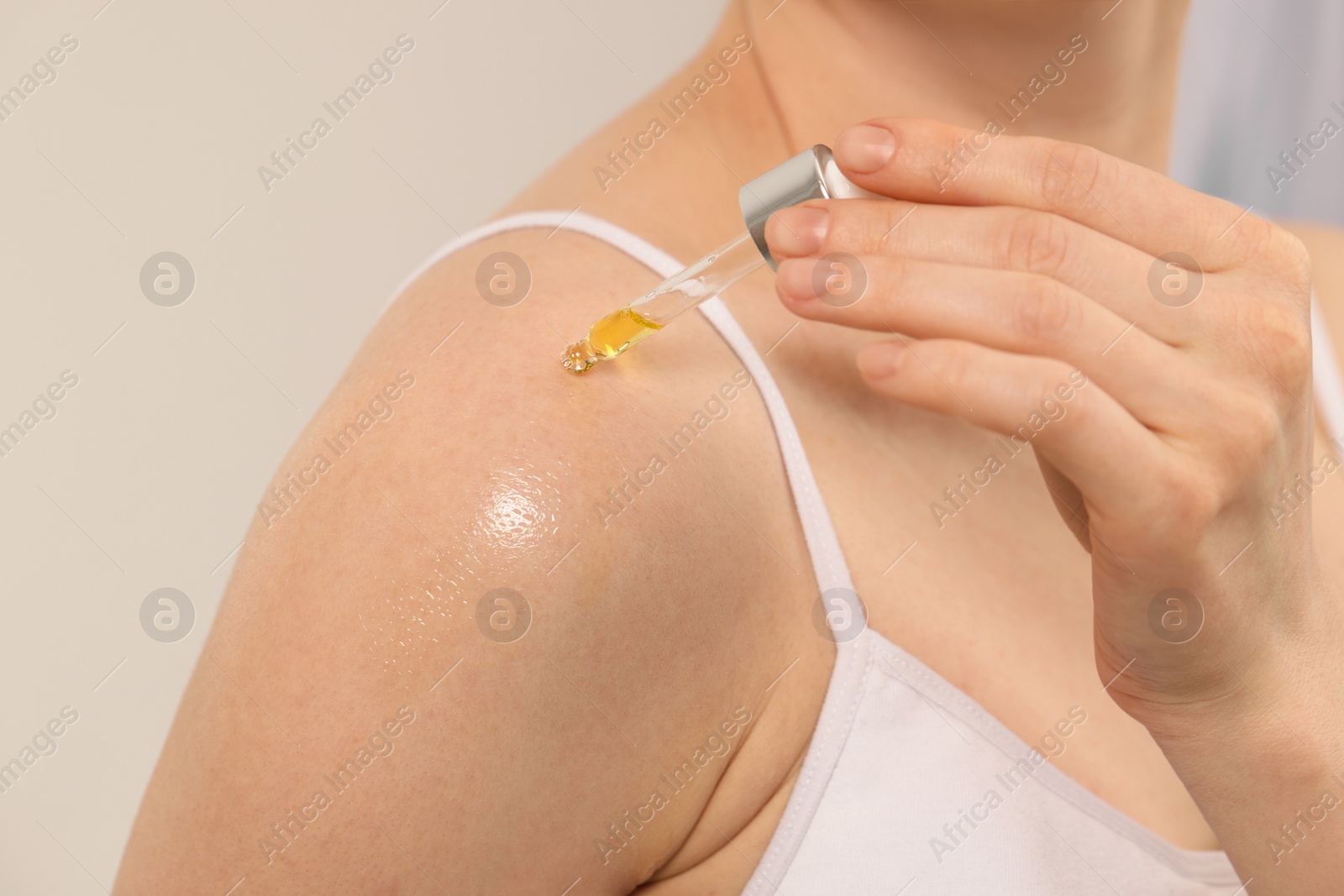 Photo of Woman applying essential oil onto shoulder on blurred background, closeup