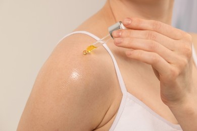 Woman applying essential oil onto shoulder on blurred background, closeup