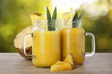 Image of Tasty pineapple smoothie in mason jars on wooden table against blurred background