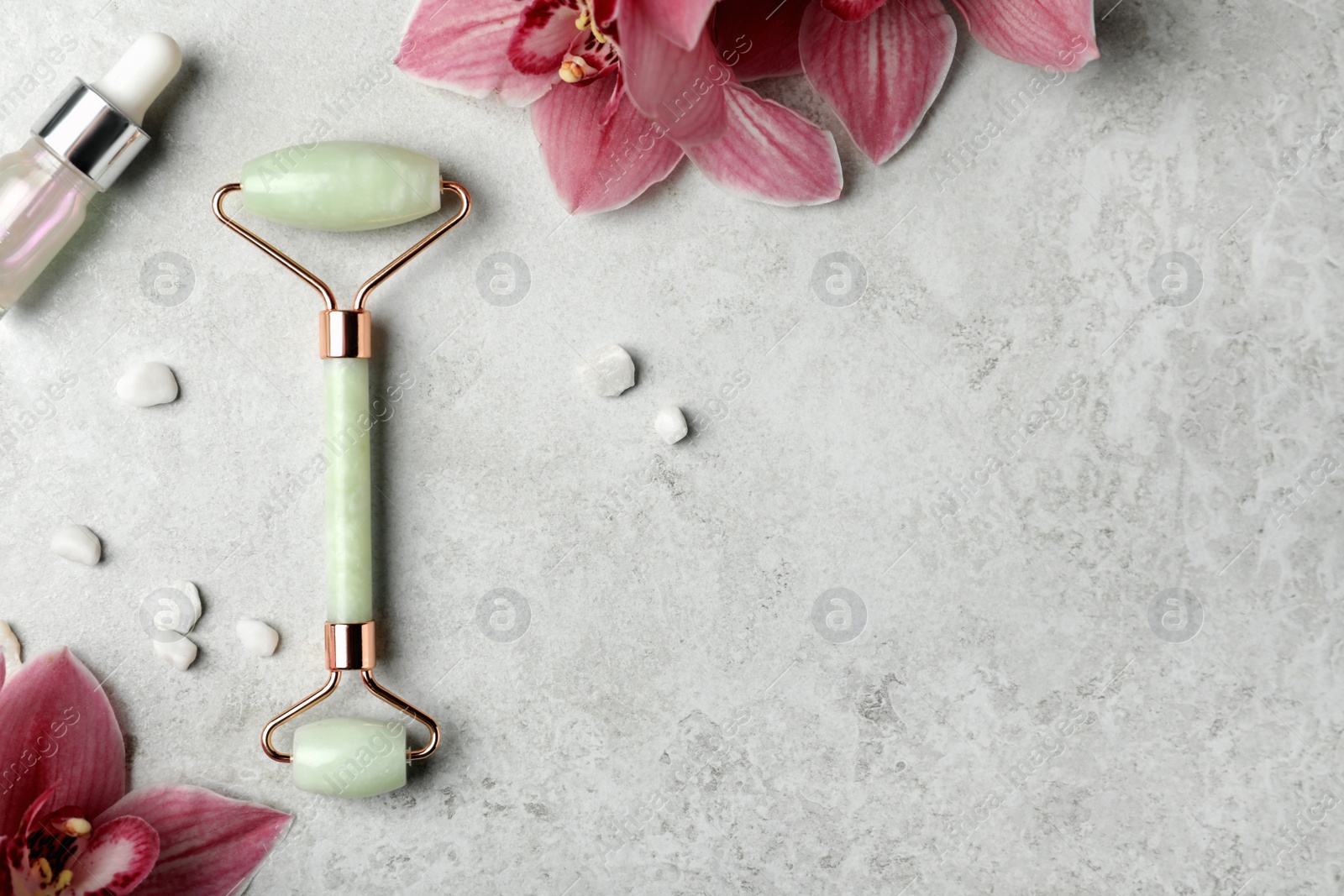Photo of Natural jade face roller, cosmetic product and flowers on grey background, flat lay. Space for text