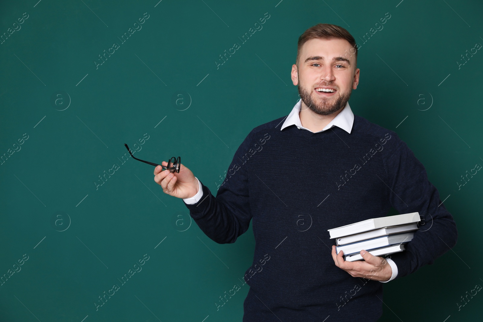 Photo of Portrait of young teacher with books and glasses on green background. Space for text