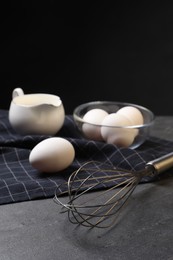 Photo of Metal whisk and raw eggs on dark grey table